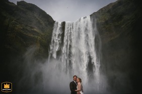 Bride and groom posing by a dramatic waterfall in Skogar, Iceland, with a graphic and striking composition.